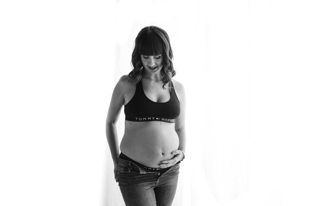 Sesión de fotos a una mujer embarazada en estudio sujetando barriga en blanco y negro